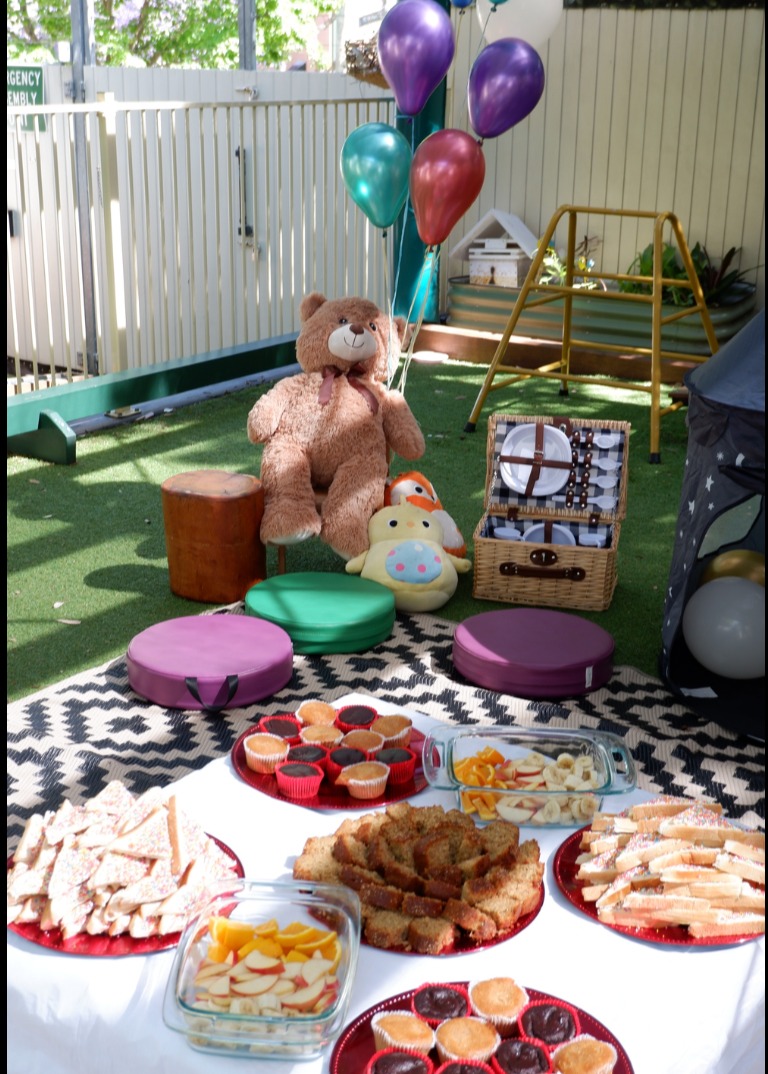 A picnic table set with fruit, sandwiches, banana bread and cupcakes for a shared celebration