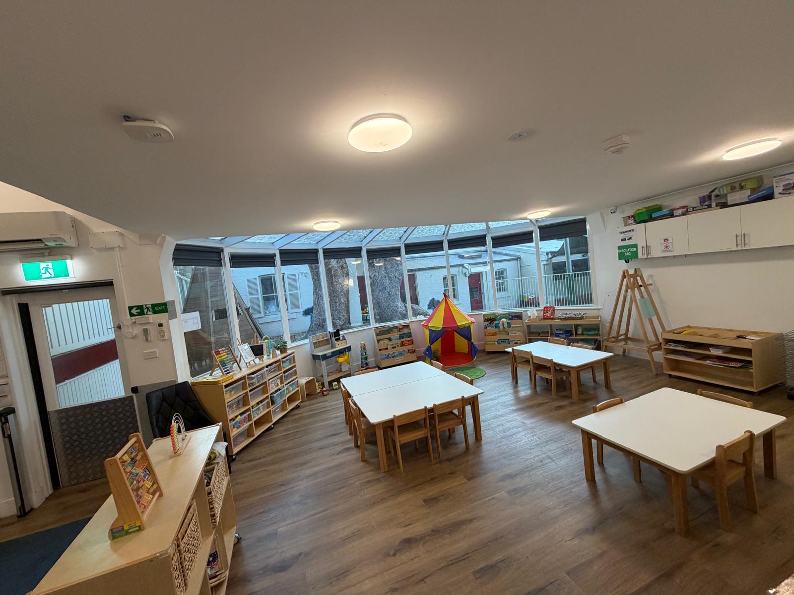 Toddler room at Little Woods Early Learning in Glebe with timber tables, play tent and open shelving